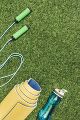 top view of arranged yellow mat, skipping rope and water bottle on green grass