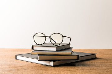 close up view of pile of black notebooks and eyeglasses on wooden tabletop