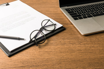 close up view of eyeglasses, laptop and notepad with pen on wooden tabletop