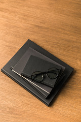 top view of pile of black notebooks and eyeglasses on wooden tabletop