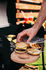 Man adjusting bun on meat of burgers cooked outdoors on grill