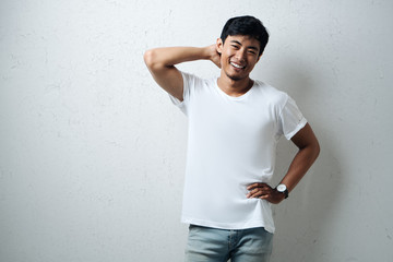 Smiling guy in white blank t-shirt, grunge wall, horizontal studio portrait