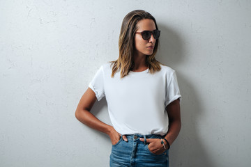 Stylish woman in white blank t-shirt wearing glasses, grunge wall, horizontal studio portrait