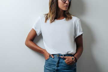 Nice woman in white blank t-shirt wearing glasses, empty wall, horizontal studio close-up