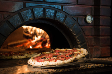 close up view of cooking process of raw pizza on wooden stove in brick oven