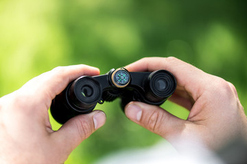 cropped shot of man holding binoculars on blurred green background