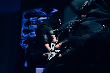 cropped shot of hacker with nipping pliers in hands with cables on background