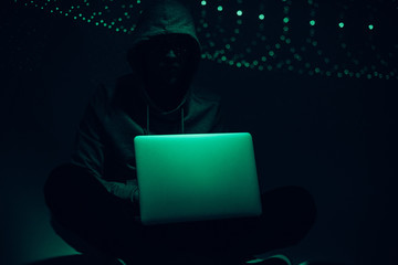toned picture of silhouette of hacker in hoodie using laptop