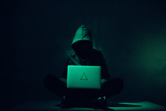 toned picture of silhouette of hacker in hoodie using laptop