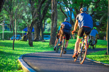 Fototapeta premium People exercise in the park. (Bicycling, jogging, walking) among green trees and tall buildings in central Bangkok. (Benjakitti Park)