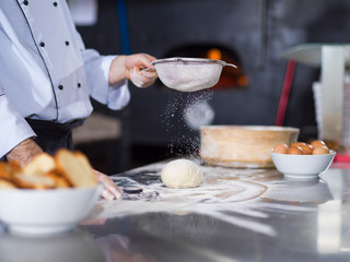 chef sprinkling flour over fresh pizza dough