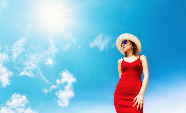 Summer time concept.Woman with sunglasses and sun hat in red dress on hot summer day with blue sky background and sun.