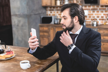 side view of handsome loner businessman taking selfie with smartphone at kitchen