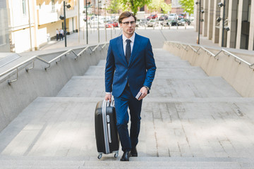 young businessman in stylish suit with luggage and flight tickets