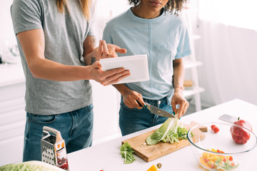 cropped shot of man pointing on digital tablet with recipe to girlfriend while she cooking at kitchen