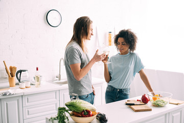 multiethnic young couple clinking wine glasses at kitchen