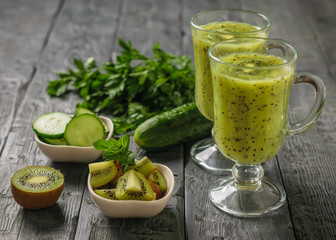 Two glasses of freshly made kiwi and cucumber smoothies on a black wooden table.