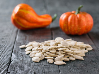 Two decorative ripe pumpkins and a bunch of pumpkin seeds on a rustic table.