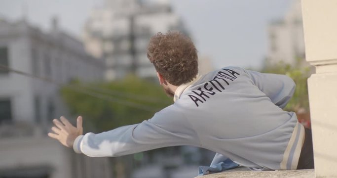 Happy Argentinian football supporter waving jersey while celebrating victory in balcony