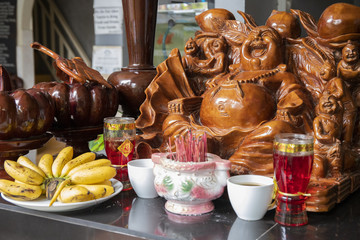 Wooden statue of laughing Buddha with scented sticks and food gifts. Wood carving art statue.