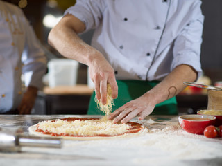 chef sprinkling cheese over fresh pizza dough
