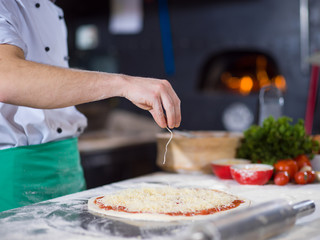 chef sprinkling cheese over fresh pizza dough