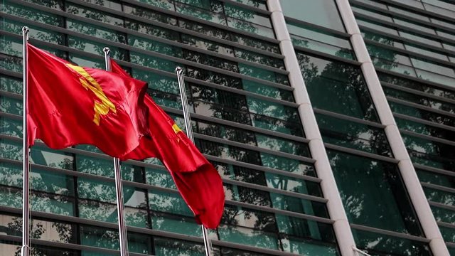 The red flag with communist symbols of a sickle and a hammer flying by building.The Red flag with a five-pointed star flutters on the pole.