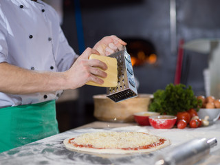 chef sprinkling cheese over fresh pizza dough