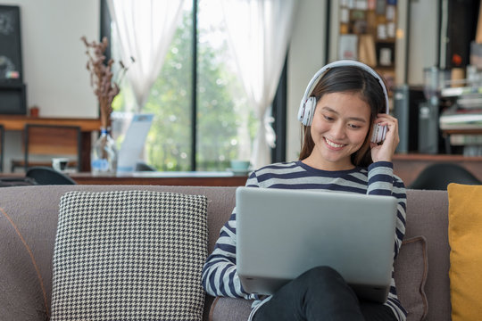 Asian teenager girl using laptop computer and listening music on sofa with happy smiling face at coffee shop,Digital age lifestyle