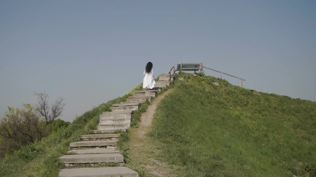 Elegance woman moves up the stairs on green hiil
