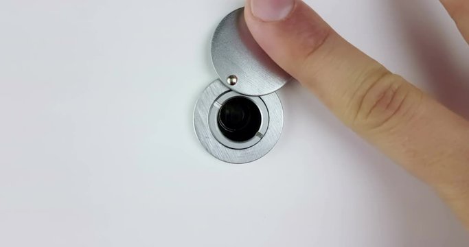 man looks through a house or hotel peephole of white door with his hand, zoom in and zoom out camera movement, check security safety spy concept