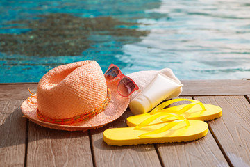 Hat, sunglasses and sunscreen at the side of swimming pool, summer travel concept