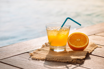 Close up of screwdriver cocktail alcohol drink with orange juice, slices and ice standing near the pool. Refreshing iced lemonade beverage in glass by the poolside. Sun glares. Background, copy space.