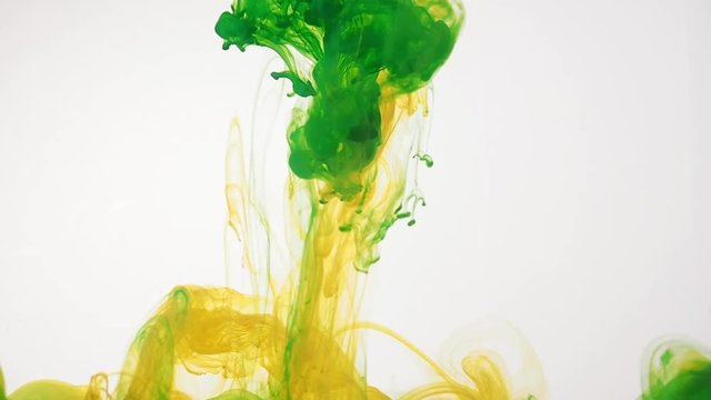 Green and yellow acrylic paint swirling in water on white background. Ink is moving mixed and intertwined creating abstract clouds. Traces of ink dissolving in water. 60fps, HD format.