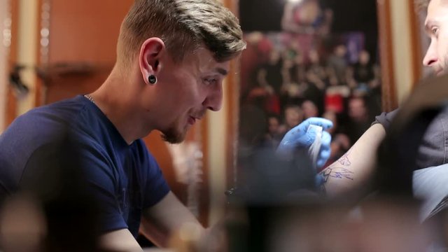 Portrait of a modern tattoo artist while working with a client. A professional tattoo artist makes a tattoo on a man's arm in a tattoo parlor.