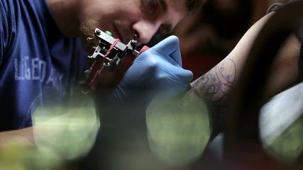 Cool tattoo master with professional tattoo machine makes a tattoo for a man in a stylish tattoo parlor.