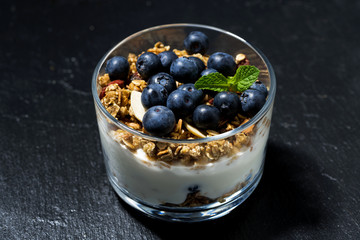 dessert with fresh blueberries, granola and cream on dark background