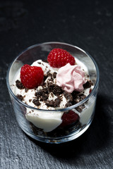 dessert with fresh raspberries, chocolate biscuits and cream on dark background, vertical