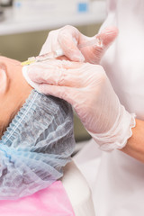 Woman getting cosmetic injection in forehead. Beautiful woman gets anti age injection in her face.