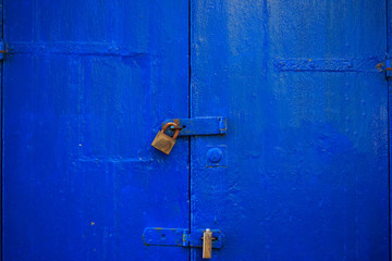 Wooden blue door background locked with two rusty padlocks. Aged, closed entrance, close up view with details.