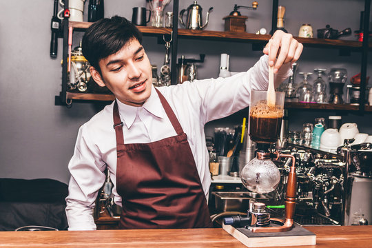 Handsome barista making coffee on syphon coffee maker in the cafe