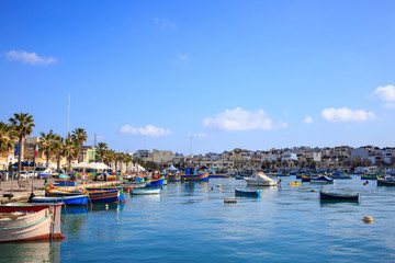Marsaxlokk historic port full of wooden boats in Malta. Blue sky and village background.