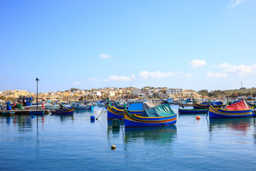 Fototapeta na wymiar Marsaxlokk historic harbor full of wooden boats in Malta. Blue sky and village background.