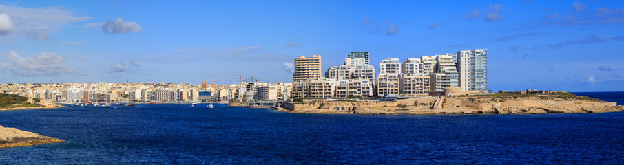 Malta, Valletta. Sliema town with multistorey buildings, blue sea and blue sky with few clouds background. Panoramic view, banner.