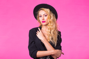 Gorgeous young blonde woman in black stylish fashionable hat posing on pink background.