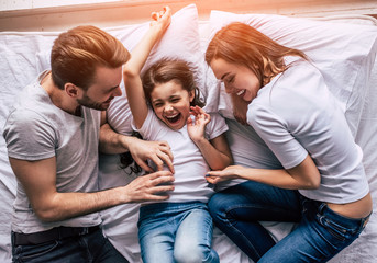 The happy daughter and parents joying on the bed