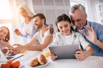 The happy family sitting with a laptop and the tablet at the table
