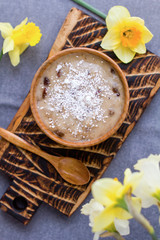 Raw vegan banana porridge with coconut and dried fruits for healthy breakfast. Morning time and summer flowers.