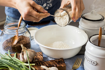 Whole wheat flour mixed with spices, herbs, greens in white bowl on fabric background in kitchen