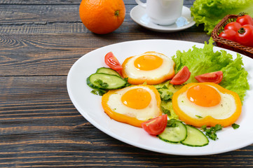 Fried egg in a circle of sweet pepper on a white plate with fresh vegetables, a cup of coffee, fresh oranges on a wooden background. Delicious healthy breakfast. Proper nutrition.